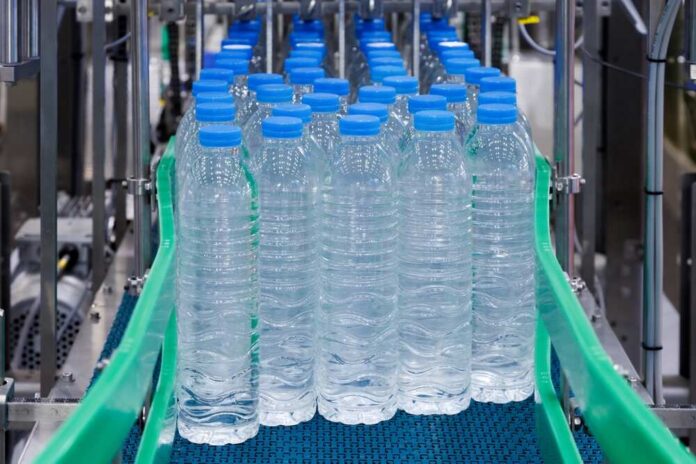 shutterstock_2492122115.jpg Conveyor belt with rows of bottled water ready for packaging