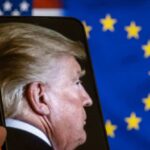 Profile view of a man displayed on a smartphone in front of American and European flags