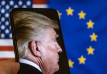 Profile view of a man displayed on a smartphone in front of American and European flags