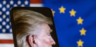 Profile view of a man displayed on a smartphone in front of American and European flags