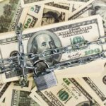 A stack of hundred dollar bills secured with a chain and padlock