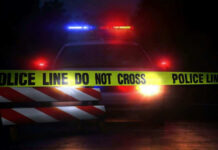 Police car with flashing lights behind caution tape.