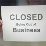 A person holding a sign that reads 'CLOSED Going Out of Business'