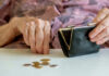 Elderly hands with purse and coins on table.