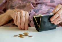 Elderly hands with purse and coins on table.
