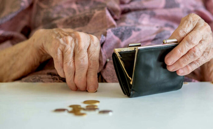 Elderly hands with purse and coins on table.