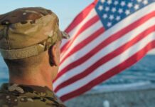 Soldier in uniform standing in front of an American flag by the ocean