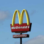 McDonalds drive-thru sign against a blue sky.