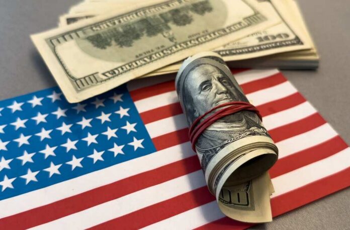 A roll of hundred dollar bills placed on an American flag