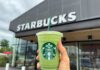 Hand holding a green matcha drink in front of a Starbucks store