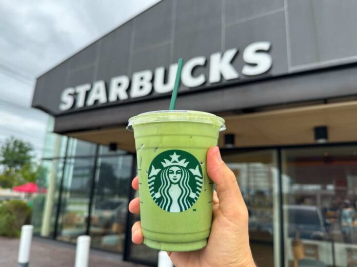 Hand holding a green matcha drink in front of a Starbucks store