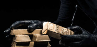 A person in black gloves handling gold bars against a dark background
