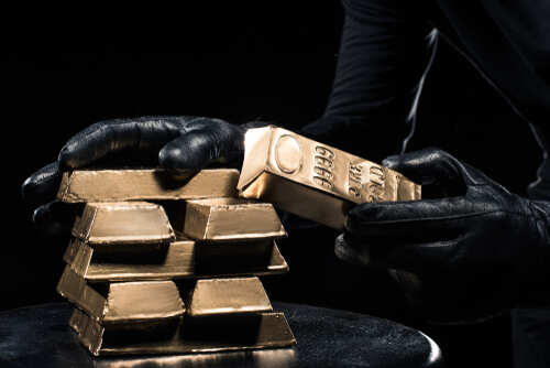 Close-up,View,Of,Golden,Bars,In,Hands,Of,Thief A person in black gloves handling gold bars against a dark background