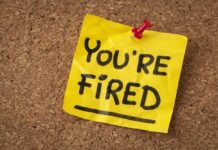 Mass Layoffs? Starbucks Cuts Hundreds! A yellow sticky note pinned to a corkboard with the words 'YOU'RE FIRED' written on it