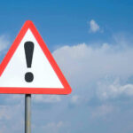 Triangle warning sign with exclamation mark against sky.