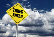 Bezos’s Tax Plan Dazzles – Can It Happen? Yellow road sign reading taxes ahead clouds background