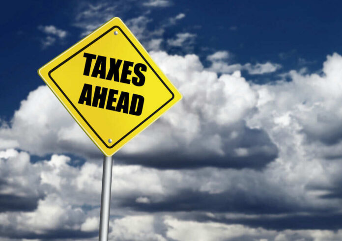 shutterstock_233717710 Yellow road sign reading taxes ahead clouds background