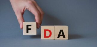 A hand holding a wooden block with the letter F, next to blocks spelling FDA