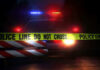 Police car with flashing lights behind caution tape.
