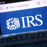 IRS Backlog From Hell Drags 20 Months Magnifying glass focusing on IRS website logo.