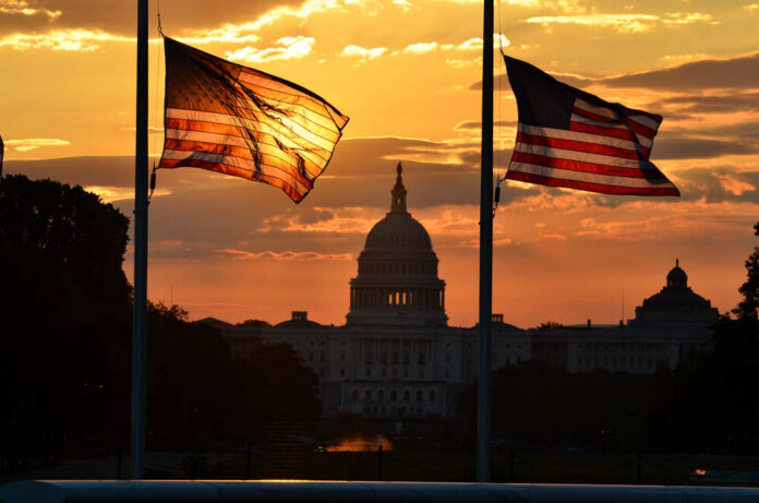 United,States,Capitol,Building,Silhouette,And,Us,Flags,At,Sunrise Silhouetted American flags in front of the Capitol building during sunset