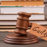 Guilty — But No Jail: Wait, What? A wooden gavel with a tag reading 'Guilty' next to stacked books