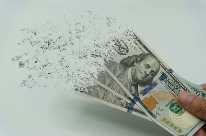 shutterstock_2122253927 Hundred-dollar bills disintegrating in hand.