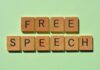 Wooden letter tiles spelling 'FREE SPEECH' on a light green background