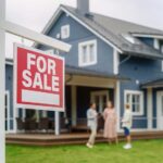 Homeownership Now Demands Six Figures?! For sale sign in front of a house with potential buyers discussing