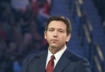 Court Injunctions Pile Up — DeSantis Declares Win Man in suit speaking at a public event.