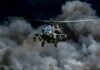 Military Apache helicopter flying through a cloud of smoke
