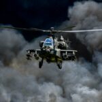 Military Apache helicopter flying through a cloud of smoke