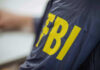 FBI’s Most Wanted Fraudster Targeted Kids Person wearing FBI jacket, letters in yellow.