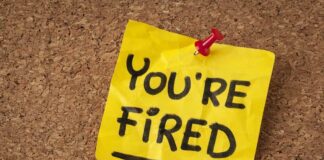 A yellow sticky note pinned to a corkboard with the words 'YOU'RE FIRED' written on it