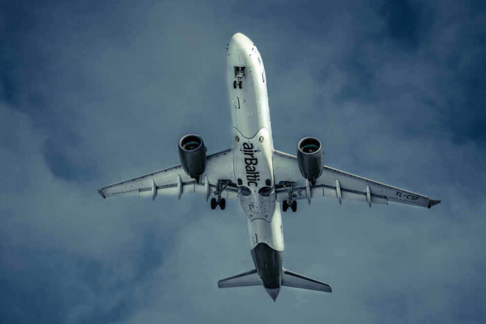 shutterstock_1907451859 Airplane flying in cloudy sky, underbelly view.