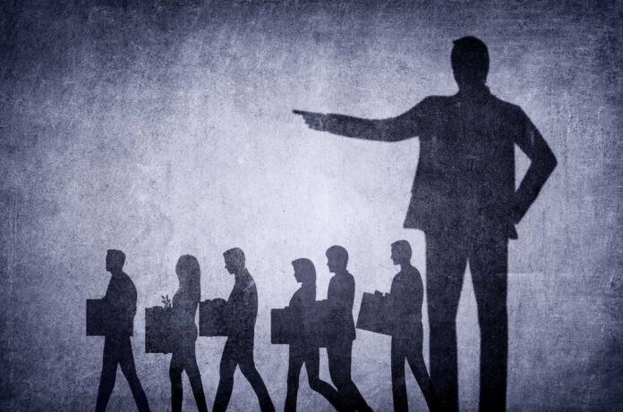 shutterstock_2254036017-1 Shadows of laid-off workers walking, large figure pointing.