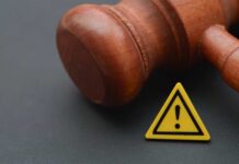 Wooden gavel with a yellow warning triangle sign on dark surface