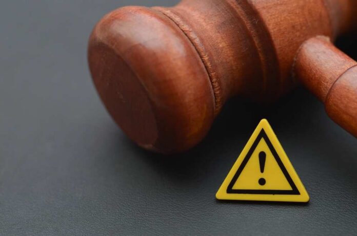 Wooden gavel with a yellow warning triangle sign on dark surface