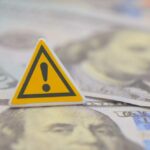 White House Aide’s $100K Crime Revealed? A warning sign placed on top of U.S. dollar bills