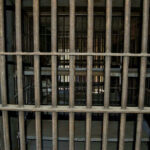 BOOM! – ICE Blitz: 10,000 Nabbed In Days Empty, rusty barred jail cell with metal bunks.