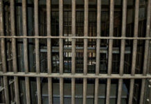 Empty, rusty barred jail cell with metal bunks.