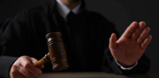 Judge holding gavel, hand raised in courtroom.