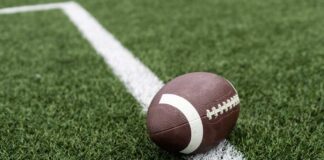 Football player kneeling on the field with a helmet beside them