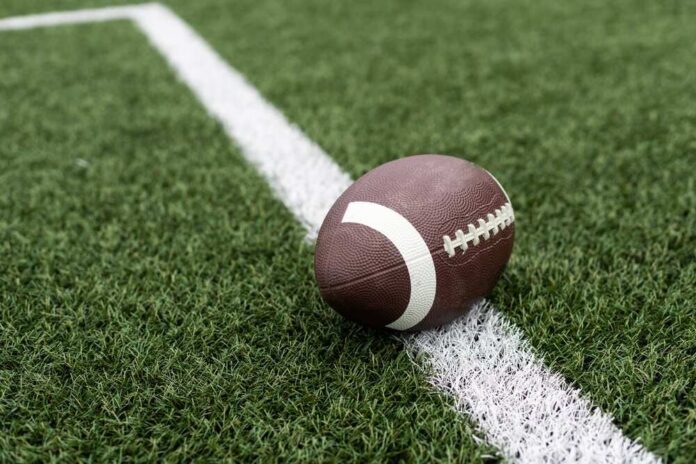 Football,On,Hash,Marks,Of,High,School,Turf,Football,Field Football player kneeling on the field with a helmet beside them