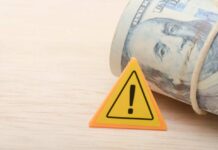 Judges Freeze Trump’s Grant Grab A roll of cash next to a warning sign on a wooden surface