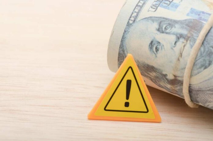 The,Warning,Sign,And,The,Money,Serves,As,A,Reminder A roll of cash next to a warning sign on a wooden surface
