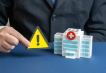 A business professional holding a warning sign next to a model of a hospital