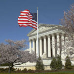 U.S. Supreme Court building with an American flag and cherry blossom trees