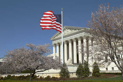 U.S. Supreme Court building with an American flag and cherry blossom trees