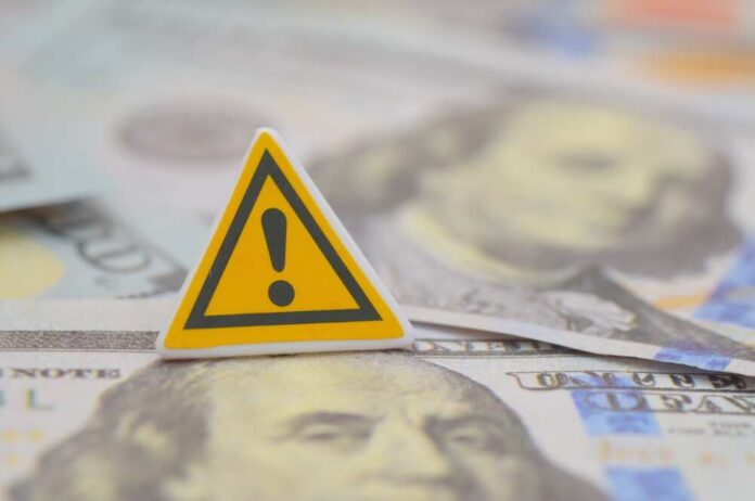 A,Yellow,Triangular,Warning,Sign,With,Us,One,Hundred-dollar,Banknotes, A warning sign placed on top of U.S. dollar bills